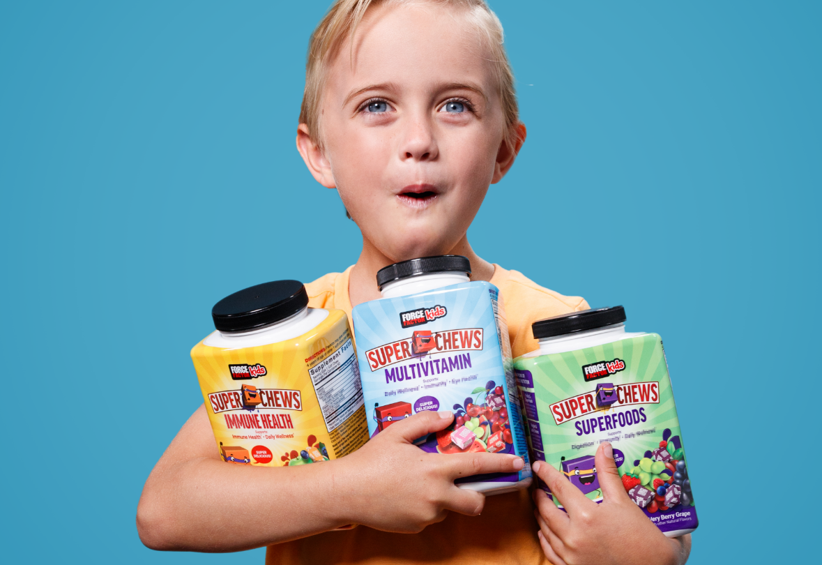 Young girl in a super hero mask and cape throwing Force Factor Kids Superfoods, Multivitamin, and Immunity Super Chews in the air.